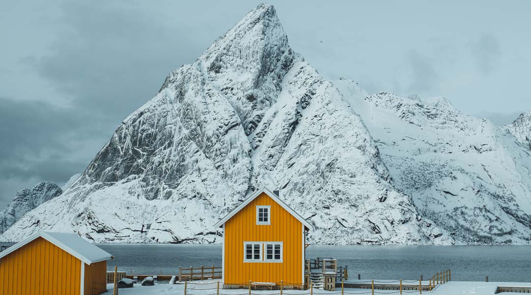 kaltwasser surfen in europa - gelbes haus vor verschneitem berg auf den lofoten